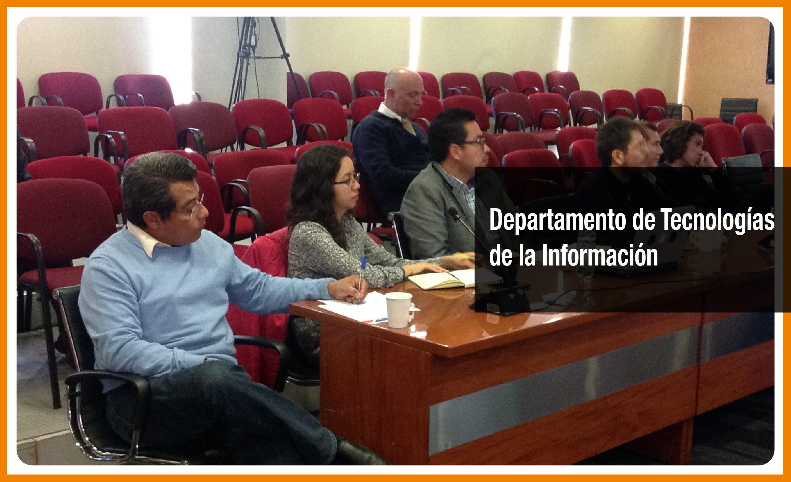 6 personas sentadas atras de una mesa viendo al frente y tomando notas. Detras ellos sillas y un hombre mirando hacia abajo